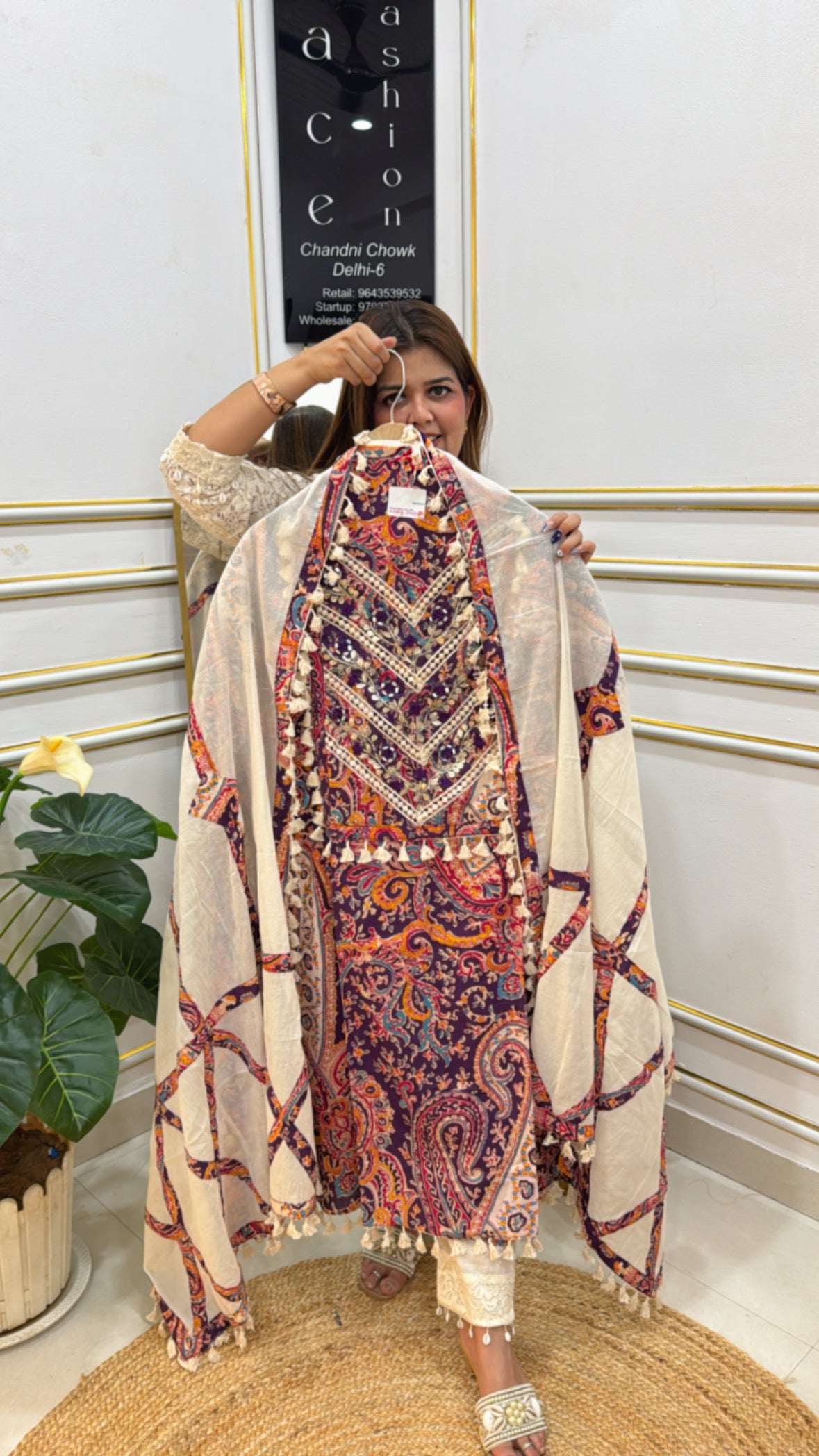 Woman holding a colorful pure cotton designer suit with intricate patterns and tassel details