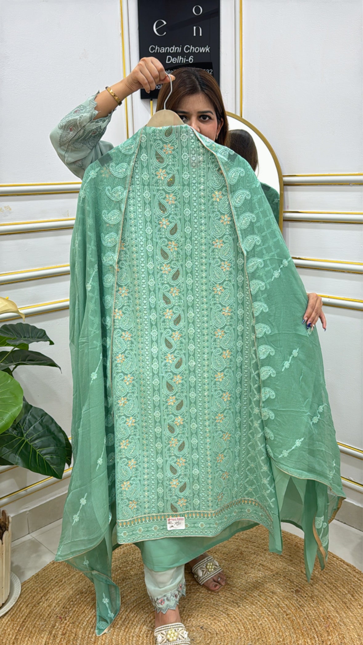 Woman holding an unstitched Lucknowi suit in green with intricate embroidery and delicate fabric details